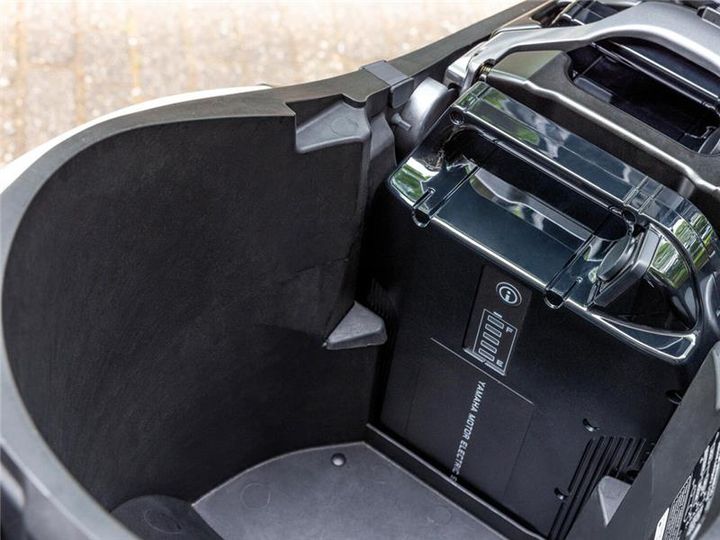A close-up view of the interior of an electric scooter's storage compartment, showcasing the battery pack and control panel within the black, molded cavity.