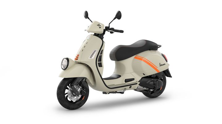 A stylish beige scooter with black and orange accents, featuring a low seat, round headlight, and retro design elements, positioned on a plain white background.