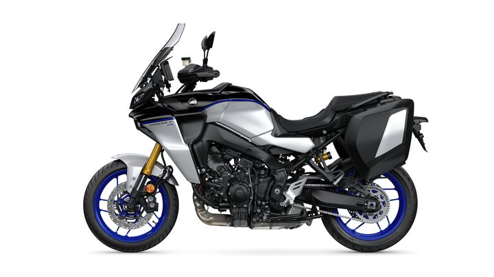 A sleek, modern motorcycle in silver and black with blue accents, featuring a prominent windscreen, rugged tires, and side panniers for storage.