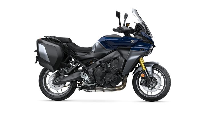 A Yamaha Tracer 9 GT motorbike is displayed against a white background, featuring a sleek design with a navy blue and silver color scheme, large saddlebags, and a tall windshield.