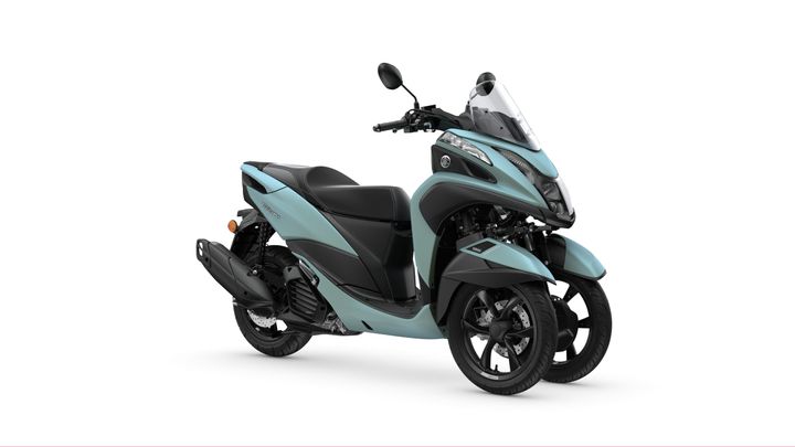 A light blue three-wheeled scooter with a sporty design, featuring a black seat and a clear windscreen, against a plain white background.