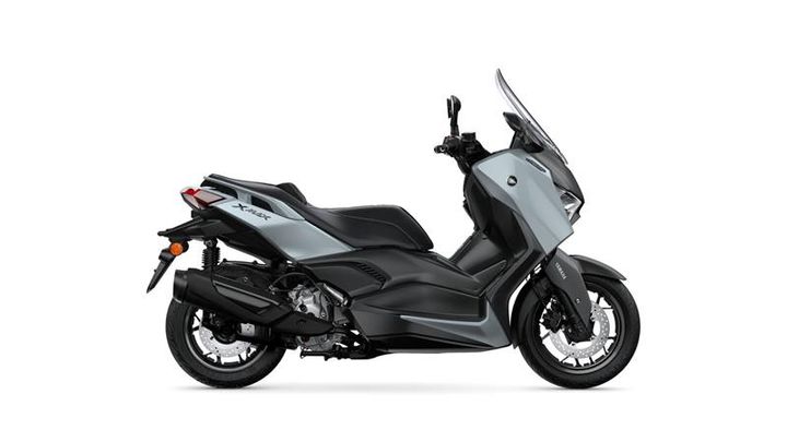 A sleek, modern scooter in silver and black is displayed from the side, featuring a prominent windshield, sporty design elements, and a comfortable seat.