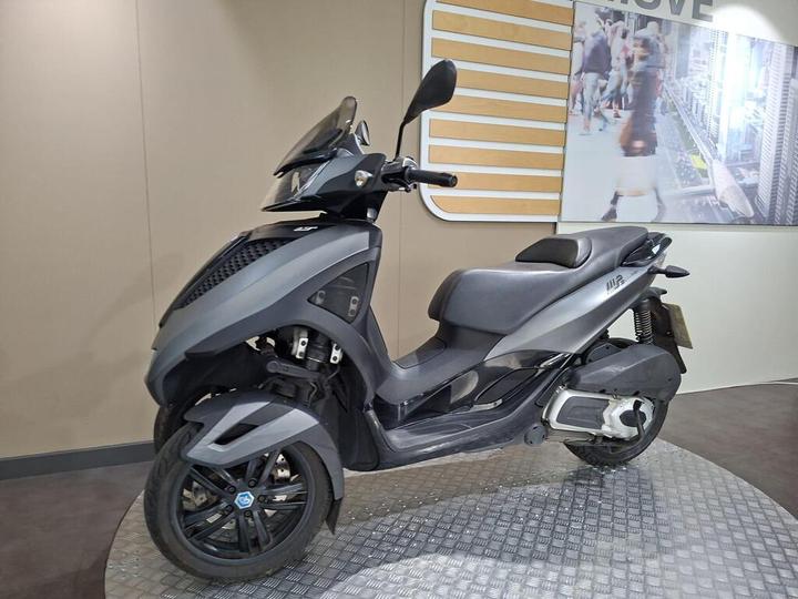 A modern, sleek gray scooter is displayed against a neutral background, featuring a protective windshield and a distinctive two-wheeled design.