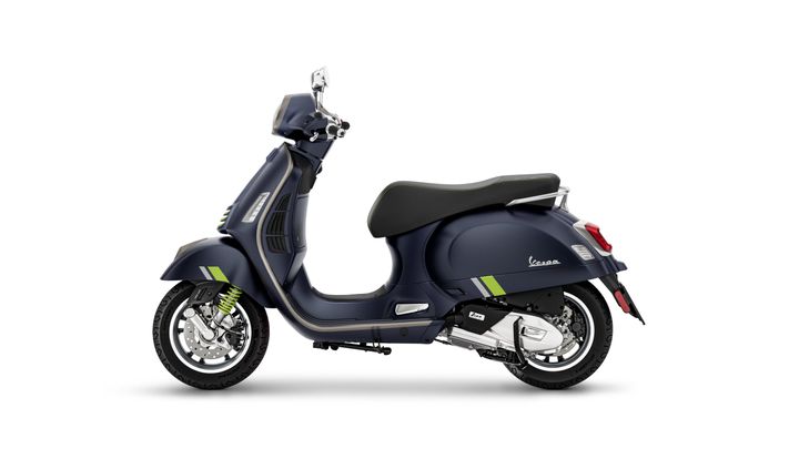 A navy blue Vespa scooter shown from the side, featuring a sleek design with green and silver accents, a comfortable seat, and chrome details. The scooter rests on a white background.