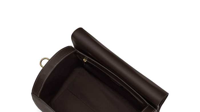 A top-down view of a brown leather bag, featuring a spacious, empty interior. The bag has a rolled top with a snap closure and two adjustable straps attached with metallic buckles.