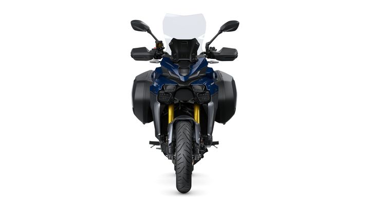 A front view of a modern motorcycle with a blue body, tall windshield, and equipped with side panniers, showcasing its large front tire and dual headlights.