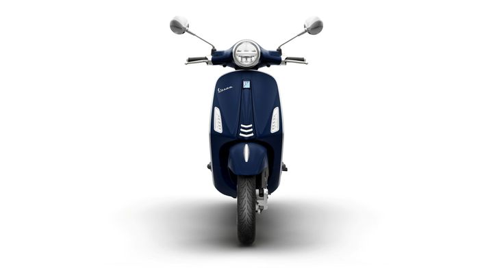 A navy blue scooter with a rounded headlight and chrome rearview mirrors, facing front with a focused shadow beneath.