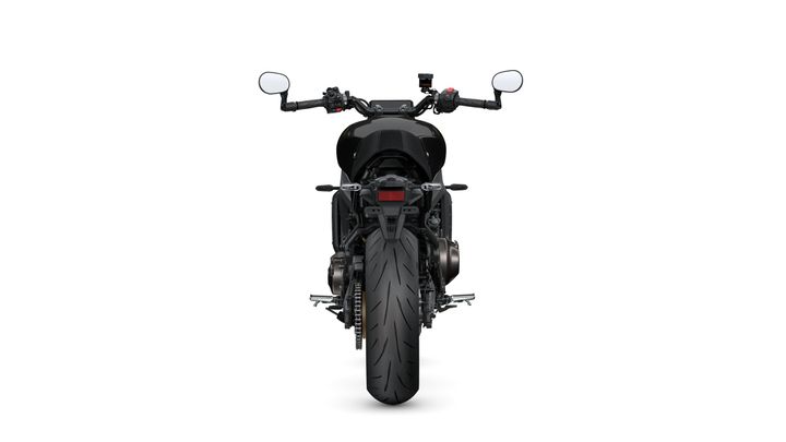 A rear view of a sleek black motorcycle, showcasing its large rear tire, dual exhaust, and handlebar controls with mirrors.