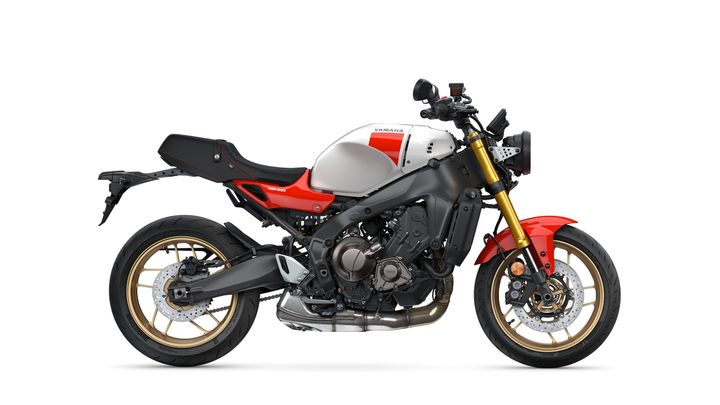 A side view of a modern Yamaha XSR900 motorcycle, featuring a sleek design with a silver and red color scheme, gold alloy wheels, and a powerful engine.