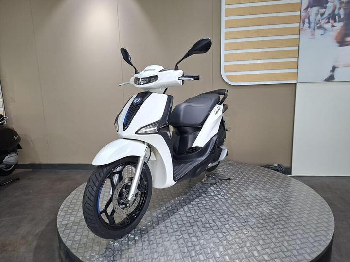 A sleek white scooter displayed on a round platform, featuring a modern design with a black seat and stylish wheels, set against a neutral backdrop.