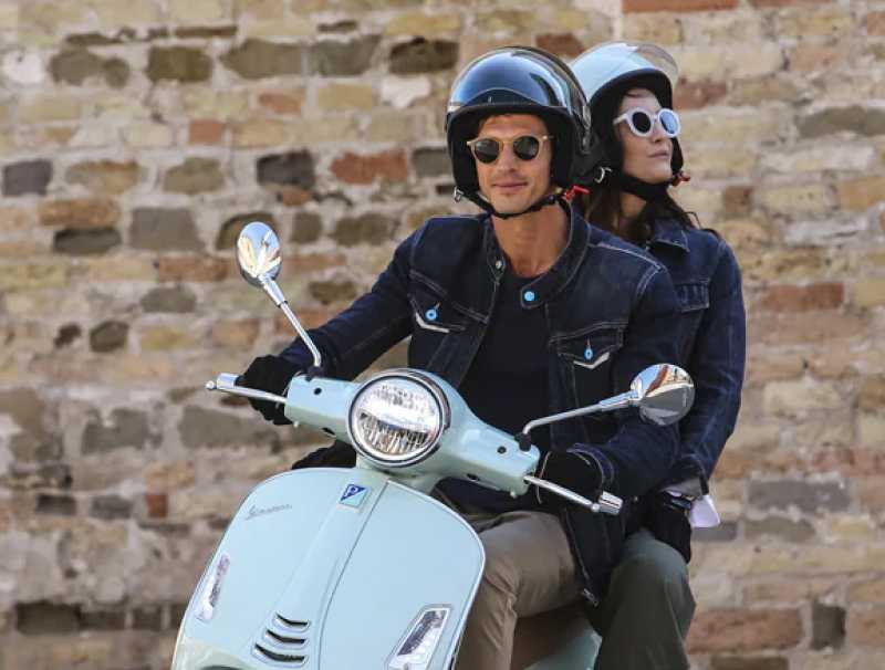 A male driving a light blue Vespa with a female passenger sitting at the back of the scooter