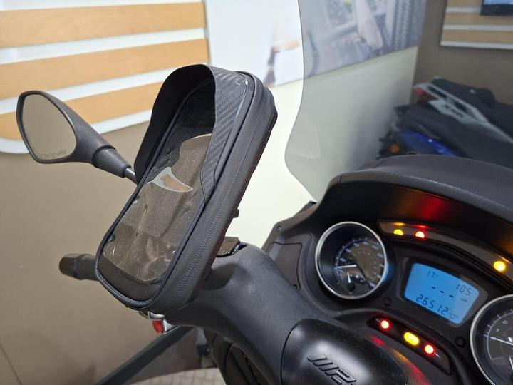A close-up of a motorcycle handlebar featuring a phone mount, side mirror, and a digital dashboard displaying information like speed and mileage.