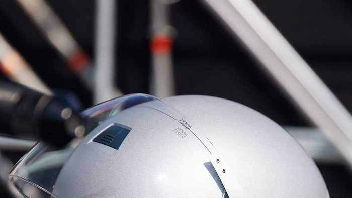 A silver helmet with green accents sits on a green padded surface, featuring a clear visor and a modern design.