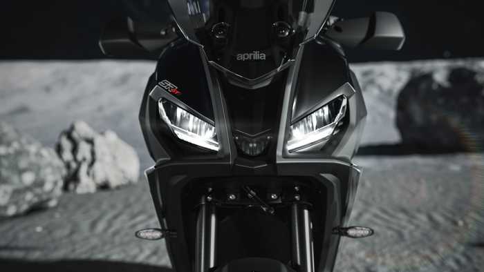 A sleek black Aprilia motorcycle is prominently displayed against a lunar landscape, with the Earth visible in the background. The bike features sharp headlights and an aggressive design, highlighting its performance attributes.