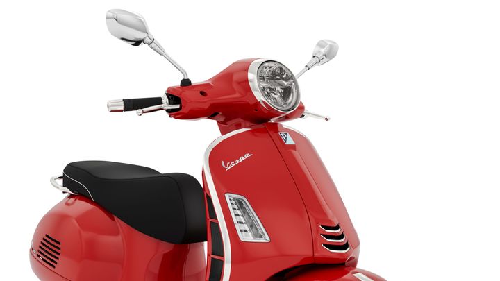 A close-up of a vibrant red Vespa scooter, showcasing its sleek design, chrome mirrors, and a black seat.