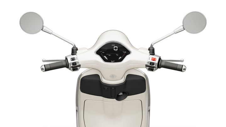 A close-up of a scooter's handlebars featuring a digital dashboard, chrome mirrors, and control levers on either side, set against a white background.