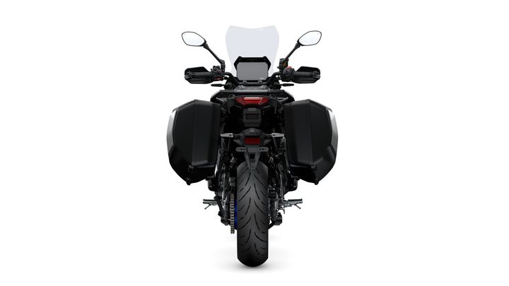A rear view of a black motorcycle with side panniers, showcasing the tire, tail light, and mirrors. The background is plain white.