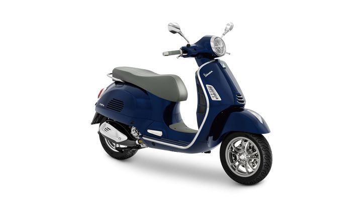 A navy blue Vespa scooter with a gray seat, showcasing a classic design and chrome accents, positioned at an angle on a white background.