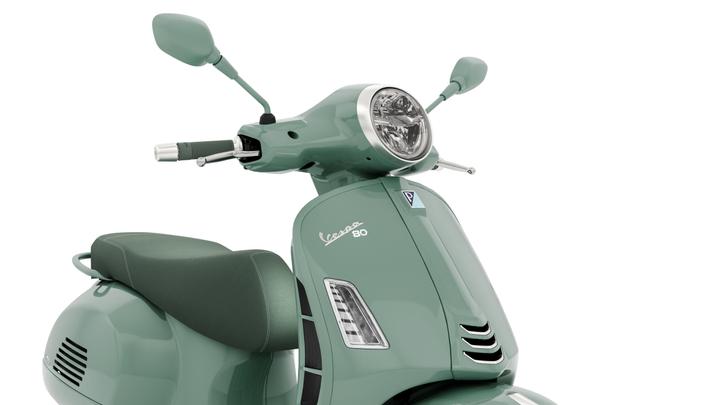 A mint green Vespa scooter featuring a round headlight, sleek body design, and a comfortable seat.