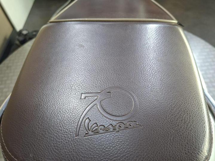Close-up of a brown textured seat featuring a debossed logo celebrating 70 years of Vespa.