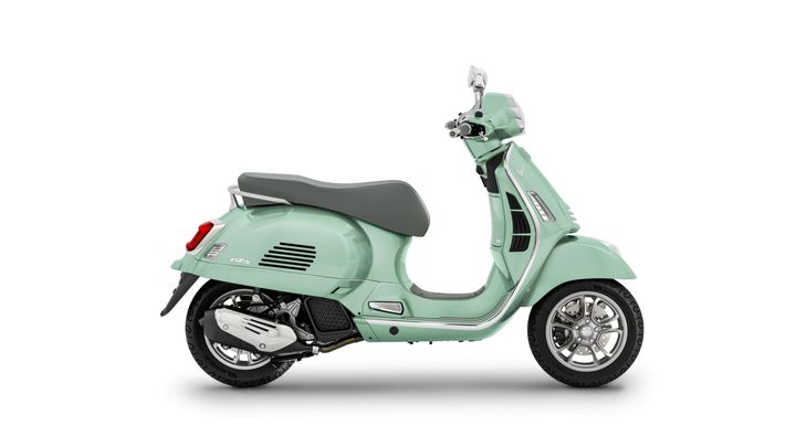 A light green Vespa scooter viewed from the side, featuring a gray seat, chrome accents, and a single headlight.