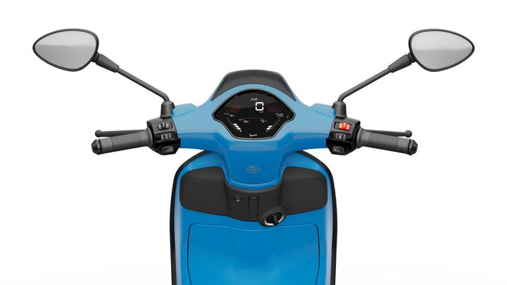 Close-up view of the handlebars and digital dashboard of a blue scooter, featuring two mirrors, grips with controls, and an illuminated display showing speed and other indicators.