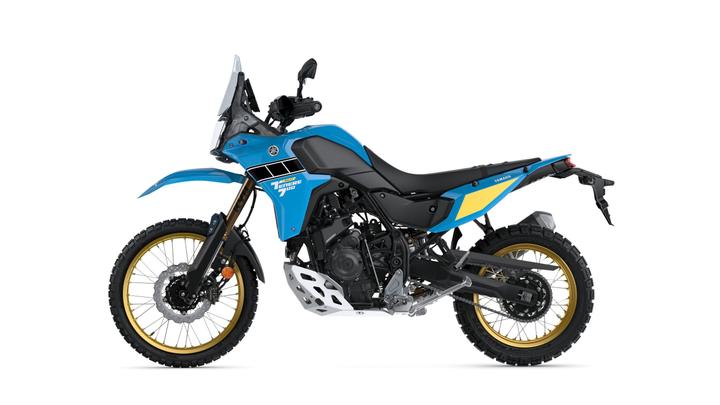 A blue and black adventure motorcycle with gold rims and rugged tires, positioned against a white background.