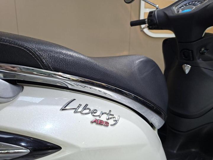 Close-up of the seat and side panel of a scooter featuring the "Liberty ABS" logo, showcasing a sleek design with a black leather seat and chrome detailing.