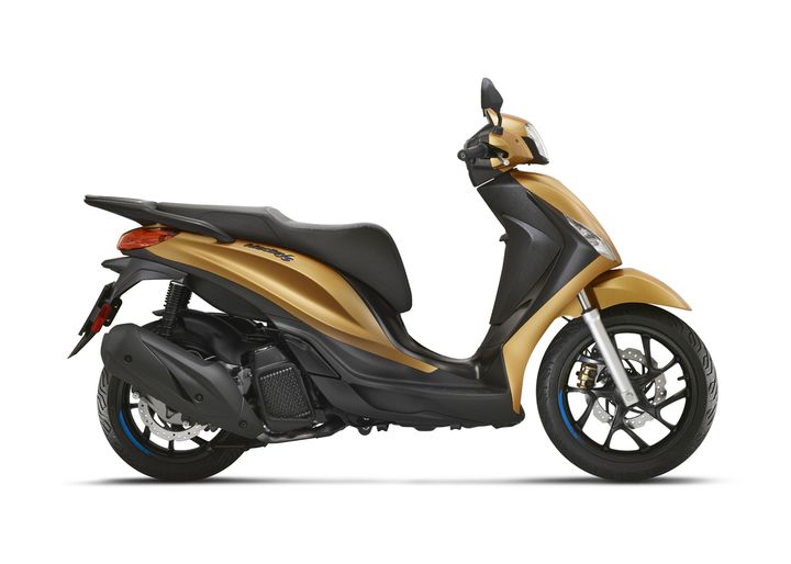 A sleek, modern scooter in a glossy gold finish, viewed from the side, showcasing its distinctive design features including a comfortable seat, stylized front headlight, and sporty wheels.