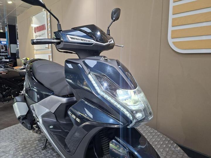 Close-up view of a sleek black Yamaha scooter, featuring modern headlights and a streamlined design, displayed in a motorcycle showroom with soft background lighting.