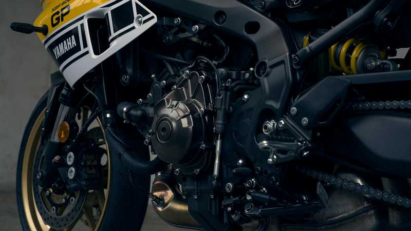 Close-up of a motorcycle engine, featuring an intricate arrangement of mechanical components, black and gold accents, and visible connections to the exhaust and frame.