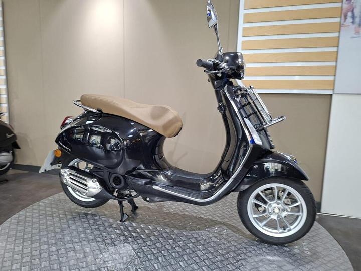 A sleek black scooter with a brown seat displayed in a showroom, set against a neutral background.