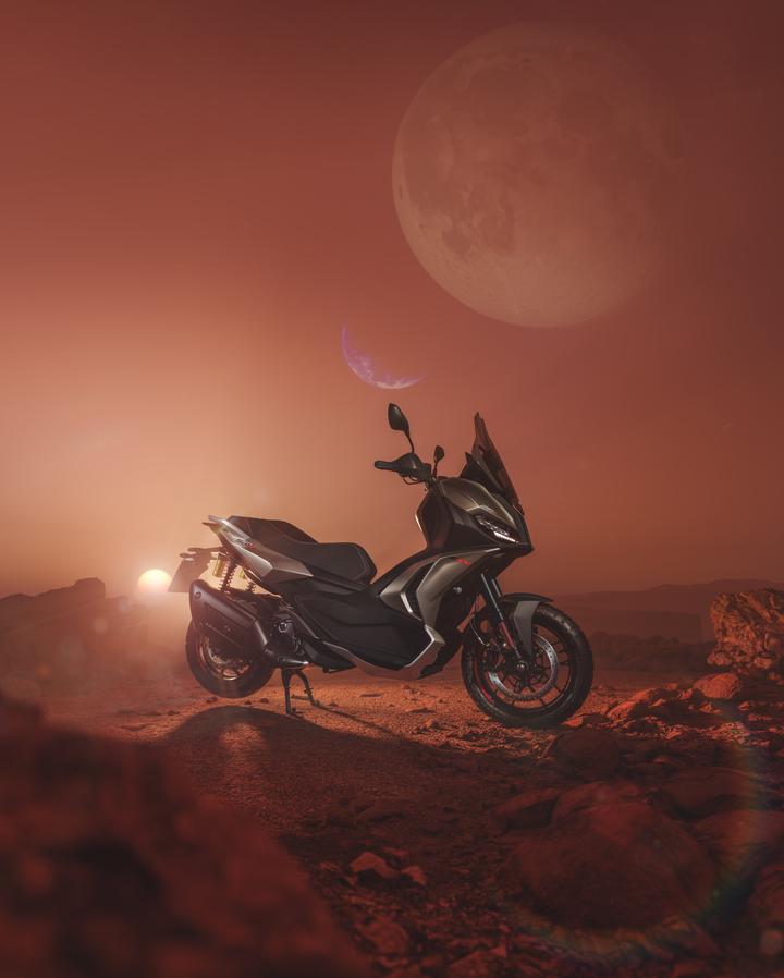 A sleek motorcycle stands on a reddish, rocky terrain under a dramatic sky with large moons and a distant sun setting.