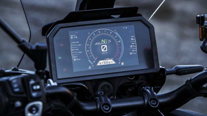 A close-up view of a motorcycle's digital dashboard displaying speed, gear, fuel consumption, and trip information, with a focus on the speedometer indicating "0 km/h" and the mode set to "STREET."
