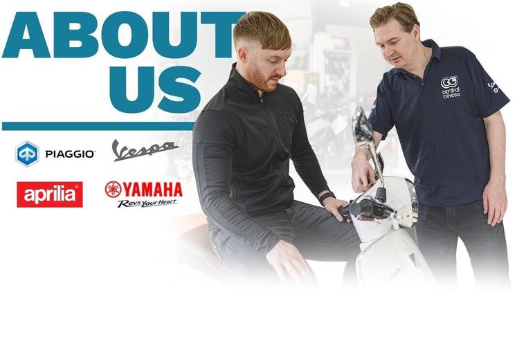 An image featuring two men interacting in a motorcycle shop. One man sits on a scooter, while the other points to the scooter's controls. The background includes blurred motorcycles. The text "ABOUT US" is prominently displayed above, along with logos of Piaggio, Vespa, Aprilia, and Yamaha.