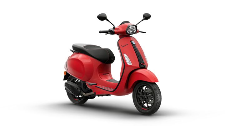 A red scooter with a sleek design, featuring a black seat, modern handlebars, and stylish wheels, set against a plain white background.