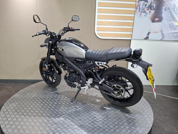 A sleek black and silver Yamaha motorcycle displayed on a circular platform, showcasing its modern design, including a low-profile seat and sporty handlebars, against a minimalistic indoor backdrop.