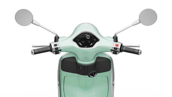A close-up view of the handlebars of a mint green scooter, featuring mirrors, a digital display, and control buttons on either side.