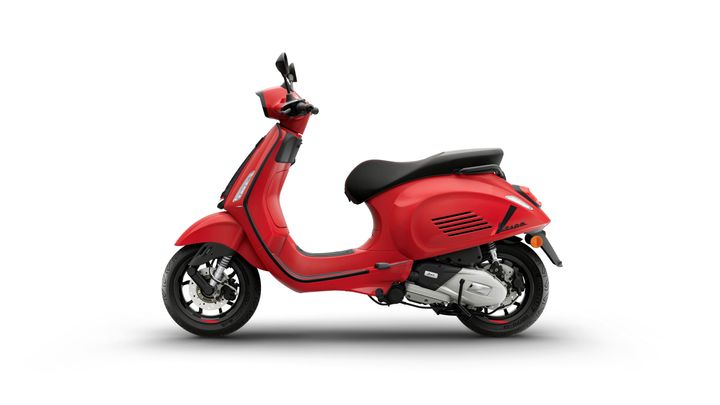 A sleek red scooter with a low-profile design, featuring a black seat and modern detailing, positioned against a white background.