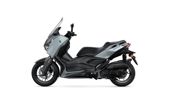 A side view of a sleek, modern Yamaha XMAX scooter in a gray and black color scheme, featuring a prominent windshield and ergonomic seat design.