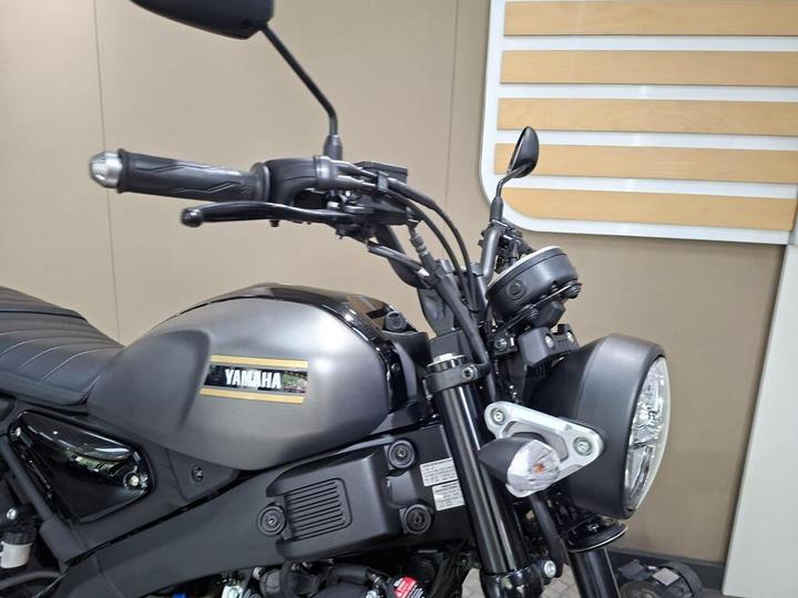 Close-up view of a Yamaha motorcycle's handlebar, showcasing the throttle grip, controls, and headlight, with a sleek black and silver design against a muted background.