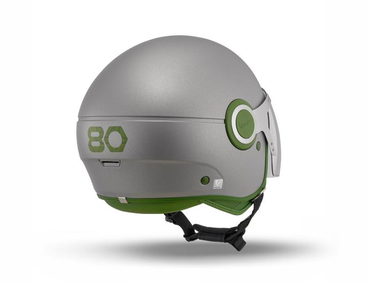 A grey ski helmet with green accents, featuring a smooth, rounded design and a chin strap, displayed from the side.