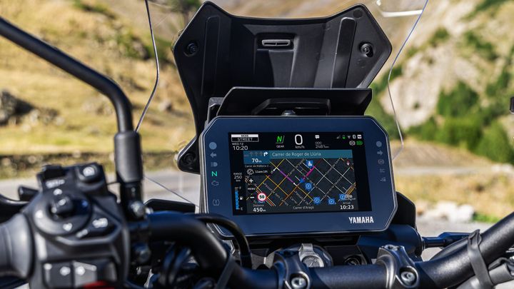 Display screen of a Yamaha motorcycle featuring a navigation map, current time, and distance to destination, with handlebar controls visible in the foreground.