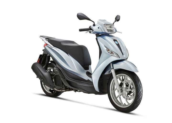 A light blue scooter with a smooth, sleek design, featuring a comfortable seat, front mirrors, and a distinctive headlight. The scooter is positioned at an angle, showcasing its wheels and stylish bodywork.