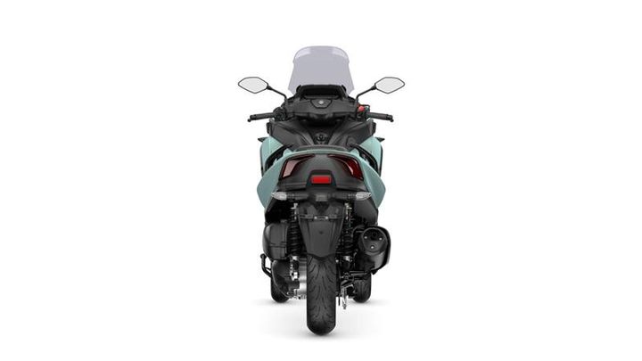 A rear view of a teal motorcycle with a high windshield, showcasing its detailed design, taillight, and exhaust.